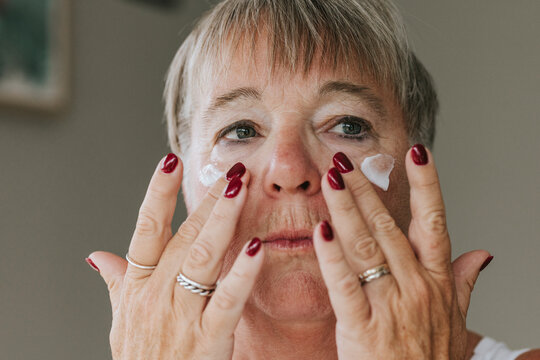 Headshot of short haired mature woman applying moisturizer on face