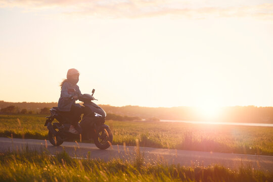 Full length of girl wearing helmet and driving scooter on scenic road at sunset