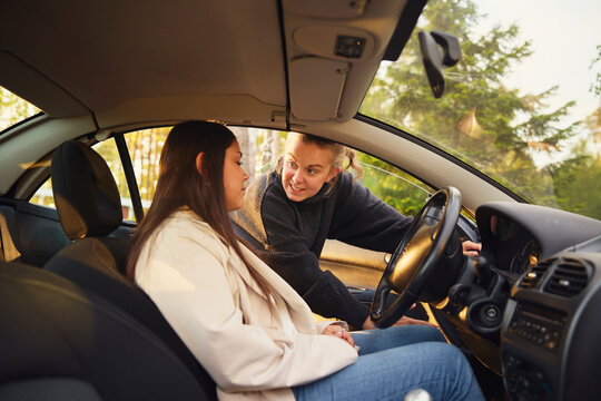 Female instructor explaining car controls to girl sitting on driver's seat