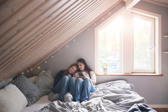 Multiracial girls spending leisure time using smart phones while sitting on bed