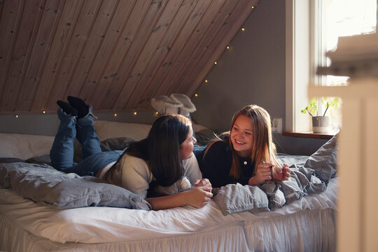 Happy girls spending leisure time talking with each other while lying on bed in attic