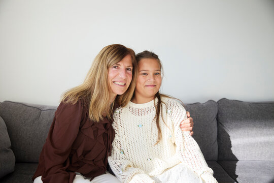 Smiling woman embracing her niece while sitting on sofa at home