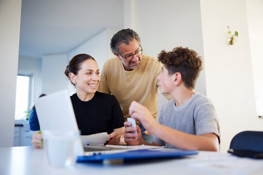 Smiling parents talking with their son studying at home
