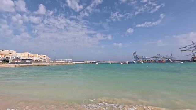 View of a marine industrial port from a sandy urban beach in Birzebbuga, Malta