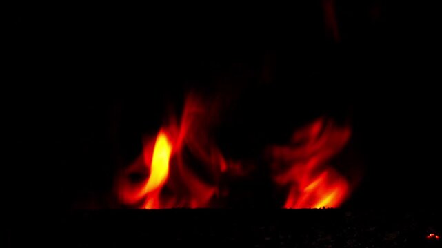 Close-up of bright flames burning inside a metal heating boiler. Dark background with subtle reflections of fire and a faint outline of the boiler door. Dramatic natural firelight and warm glow.