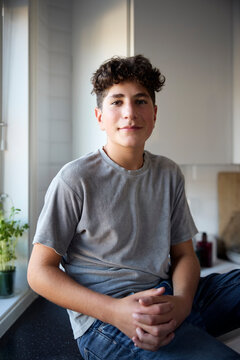 Portrait of smiling boy with hands intertwined sitting in kitchen at home