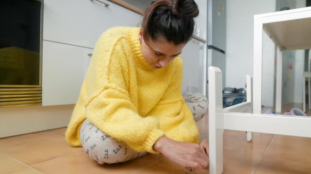 Woman Searches Floor. Young Woman On Tiled Floor Carefully Seeking Tiny Missing Item Near Furniture Leg