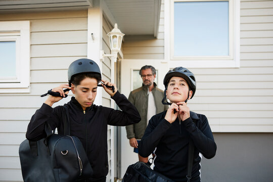 Brothers fastening helmets outside house