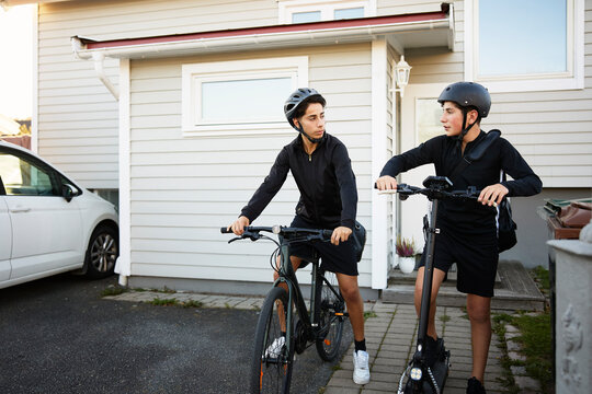 Full length of brothers commuting through bicycle and electric scooter