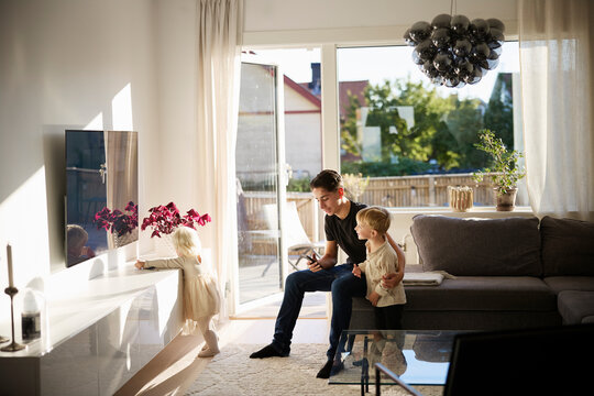 Boy watching TV with siblings sitting in living room at home