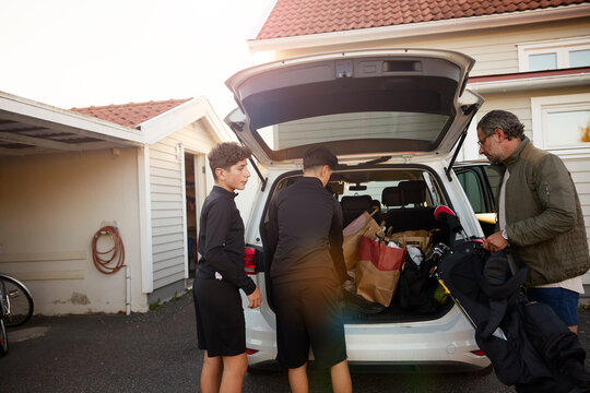 Father and sons loading bags in car trunk