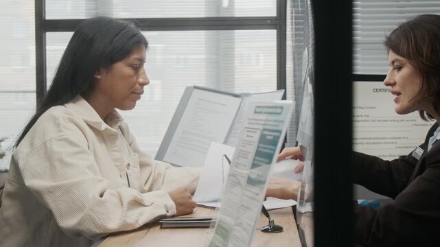 Medium side shot of polite mature Caucasian female embassy officer explaining to Hispanic customer mistakes in visa application for making corrections, while processing documents