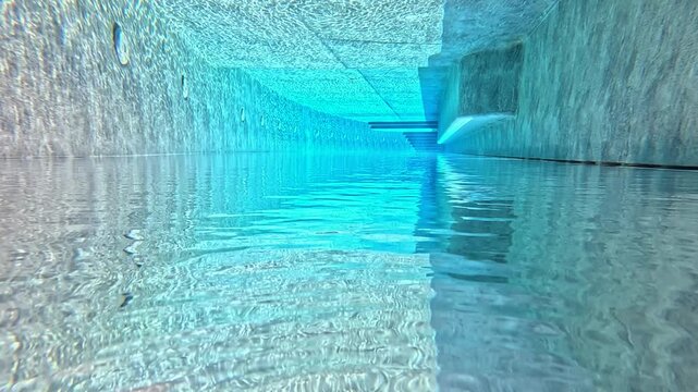 The underwater expanse of a pool shimmers with sunlight filtering through the surface, slow motion
