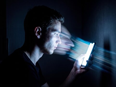 Young man staring at glowing smartphone screen, blue light, technology, addiction