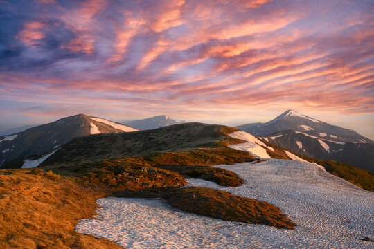Stunning sunset in spring mountains. Snow-capped hills and purple sunset sky. Ukrainian Carpathians. Landscape photography