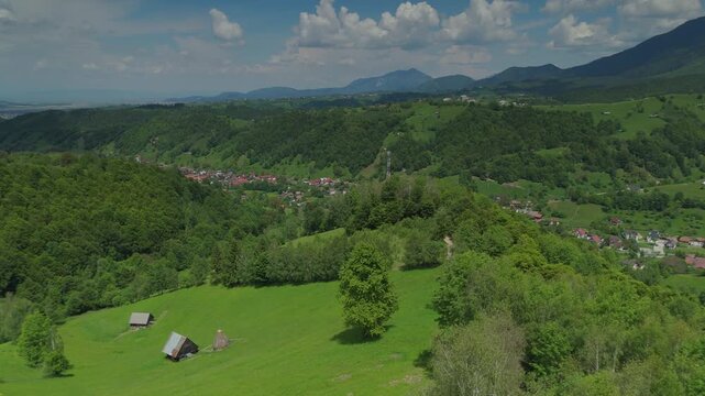 Idyllic rural scenery with rustic wooden barns on fresh green meadows overlooking Simon village and distant mountains, slow aerial descent to dirt road