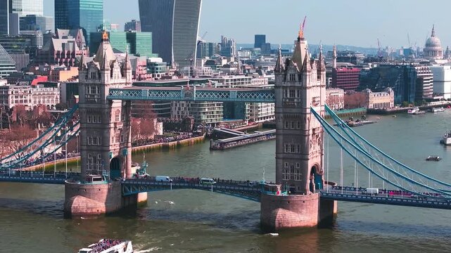 Elevated daytime view of Tower Bridge spanning the River Thames in London, with sightseeing boats, riverside activity, and the modern City of London skyline in the background.