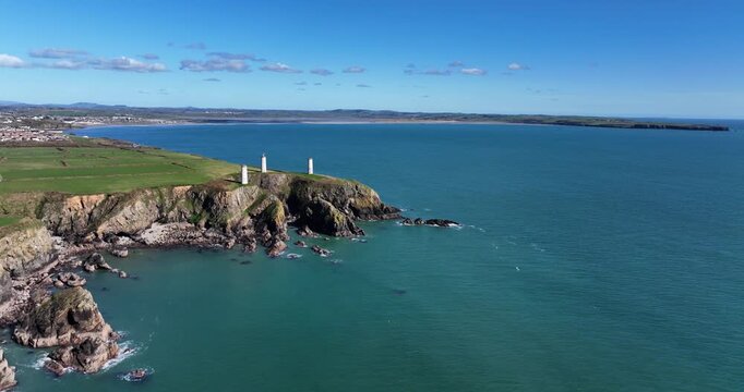 Drone circling Metalman towers with Tramore Town and Bay rocky entrance to the bay shipwreck site and towers a warning to shipping of danger on a calm spring morning