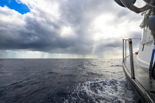 View from a boat deck of a storm approaching over the sea with sun rays and rain