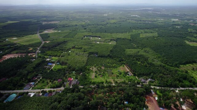 Aerial drone shot capturing expansive green farmland and rural countryside in Thailand, featuring agricultural plots, scattered homes, and road networks stretching across the landscape.