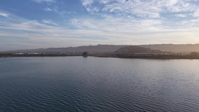 Morning sunlight illuminating the calm waters and shoreline in Berkeley, California. With wispy clouds floating in the beautiful blue sky above the coastal hills