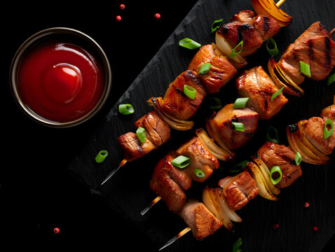 Grilled pork skewers with onions and green onions on a black slate board