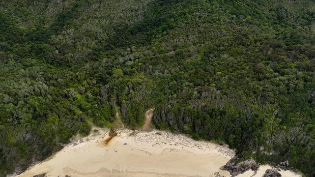 Aerial drone video flying backwards from Cape Hawke to reveal McBrides Beach in Forster. The perspective showcases rugged coastline, ocean water and natural coastal landscape