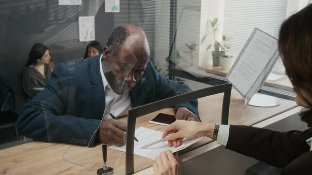 Medium shot of female consular officer assisting African American businessman in correcting mistakes in visa application form, pointing to places for signature on blanks