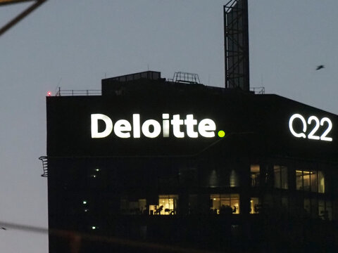 Close up of a bright white Deloitte corporate logo on a dark glass building