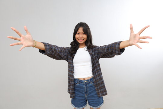 Beautiful smiling teenage girl giving a hug, stretching her arms forward to be hugged, asking for a caress, wanting to hold something, standing isolated on a gray background.