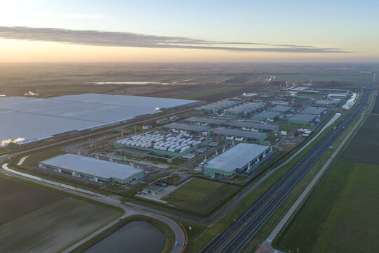 Aerial view of sprawling data center complex providing essential digital infrastructure, situated beside a highway amidst rural landscape during sunrise, Middenmeer, Netherlands.