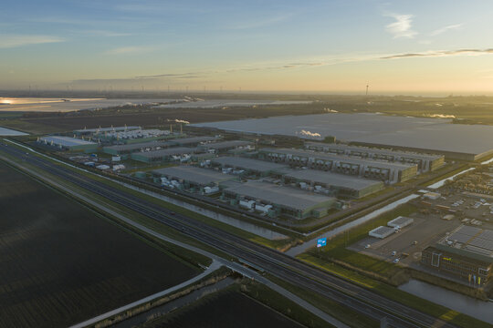 Aerial view of expansive data center park with multiple buildings alongside a highway, surrounded by fields and waterways under morning light, Middenmeer, Netherlands.