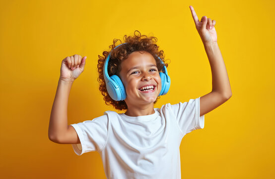 Happy Black boy dances joyfully wearing blue headphones, listening to music. Young child moves energetically with raised arms on a bright yellow studio background, expressing pure fun.