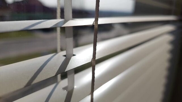 Close-up of white horizontal window blinds with sun rays and shadows