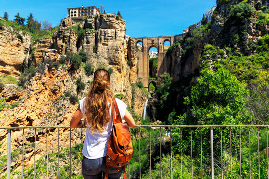 Female traveler with leather backpack admiring the iconic Puente Nuevo bridge and Tajo gorge in Ronda, Andalusia, Spain - Scenic travel and discovery concept.