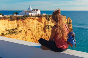 Woman sitting on a wall admiring the Chapel of Nossa Senhora da Rocha on a cliff edge, Porches,...