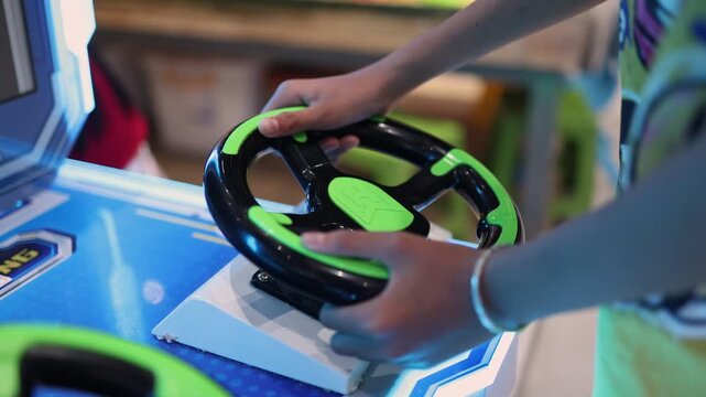 Close up of a child hand holding a steering wheel of an arcade game machine. Boy playing car racing simulator in an entertainment center. Fun leisure activity and hobby for kid concept.