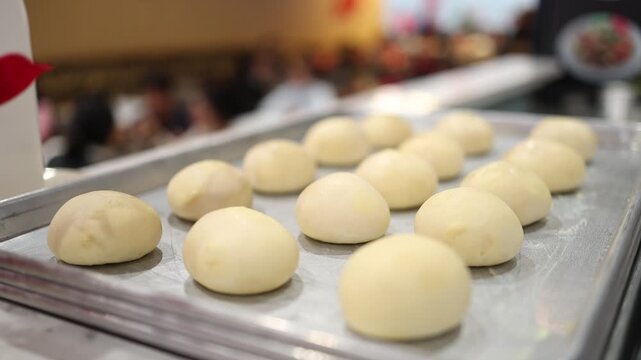 Raw dough bun for banh bao on a metal tray in a cafe. Steamed pork bun preparation in a supermarket. Asian cuisine cooking process and white bread yeast dough ball on a baking sheet.