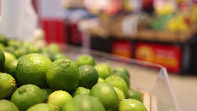 Close up of fresh green limes on a shelf in a supermarket. Pile of organic citrus fruit in a grocery store. Healthy nutrition and natural acidic ingredient concept for food and drink.
