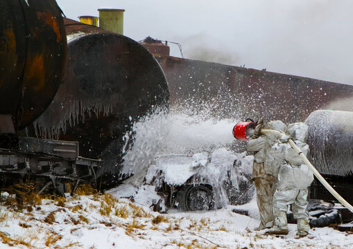 Firefighters spray foam on a large tank after a train derailment in snowy conditions