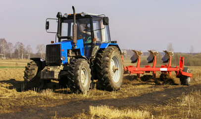 Fototapeta premium Farmer uses tractor to plow field during daytime in rural area