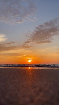 Golden hour glow over the tranquil ocean horizon as the sun sets, casting warm reflections on the sandy beach