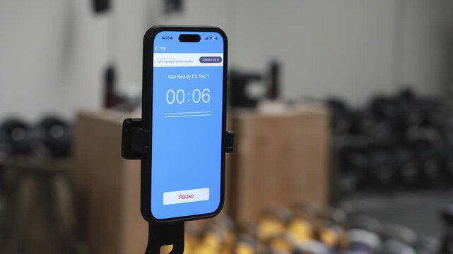 Smartphone timer on tripod in gym during workout session, fitness training concept with mobile app countdown and exercise routine tracking