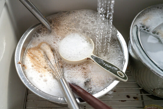 Soapy water and baking dishes being cleaned in kitchen sink close up

