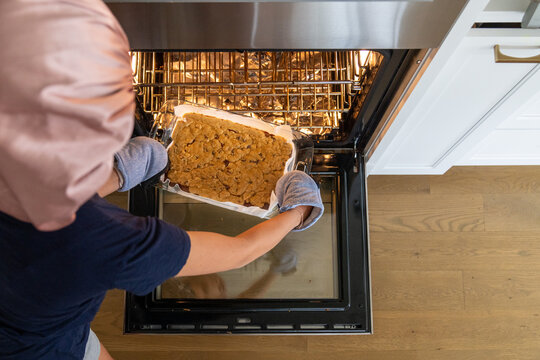 Removing freshly baked brownies from oven with oven mitts in kitchen