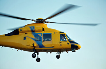 Fototapeta premium Yellow emergency helicopter with blue stripes flies against clear sky. Pilot visible in cockpit, rotor blades spinning fast, ready for medical mission.