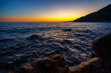 Obraz premium Atmospheric sunset over the dark waters and rocky coast of Petrovac, Montenegro. Dramatic summer travel scene.