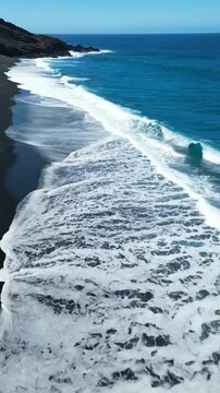 Top view of deserted black volcanic beach with waves and blue water in Coa b VSRExport