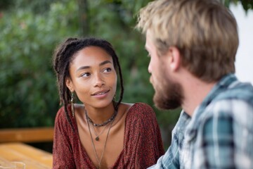 Fototapeta premium African female young caucasian male young engaged in conversation at outdoor table listening intently warm natural setting bohemian style jewelry