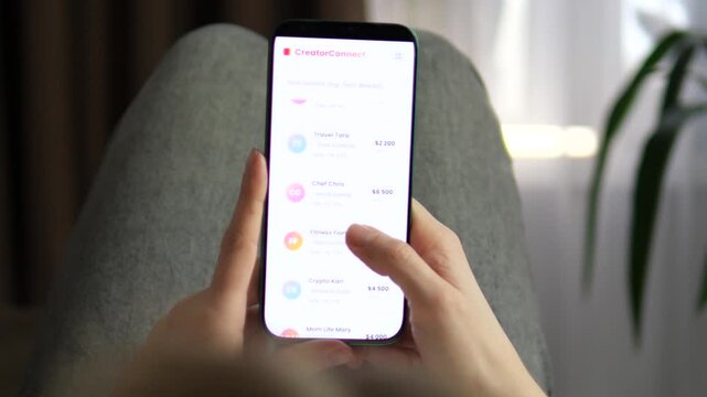 Smartphone Interface for Social Media Influencer Booking. Hand scrolling through an influencer database on a phone. Visualizing brand outreach and influencer recruitment. 